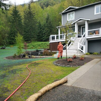 Hydroseeding process at residential Washington state home with lush green backdrop.